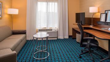 A hotel room with a sofa, a desk with a chair, a small round table, a TV, and a window with curtains.