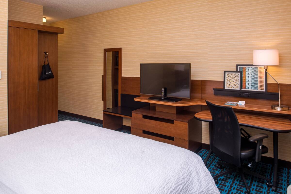 A hotel room with a bed, a desk with a computer, a TV, and a lamp.