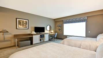 Habitación de hotel con dos camas, un escritorio con computadora, televisor, lámpara y ventana con vistas.