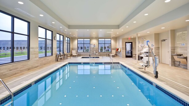 A large indoor swimming pool with clear windows, a reception area, and a view of the outside. - Hampton Inn Livonia Detroit (Livonia)