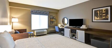 A hotel room with a large bed, a desk with a computer, a TV, and a window with a view.