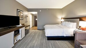 A hotel room with a bed, bedside table, lamp, TV, and a desk with a microwave. - Hampton Inn Livonia Detroit (Livonia)