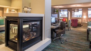A modern hotel lobby with a fireplace, comfortable seating, and a desk area. - Residence Inn St Louis Westport (Maryland Heights)