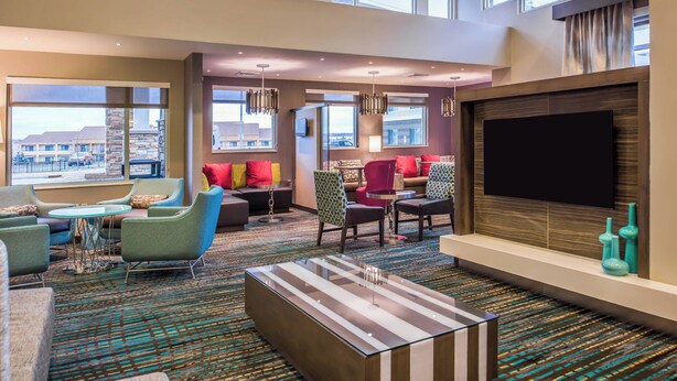 A spacious hotel lobby with a large TV screen, comfortable seating areas, and large windows offering city views. - Residence Inn St Louis Westport (Maryland Heights)