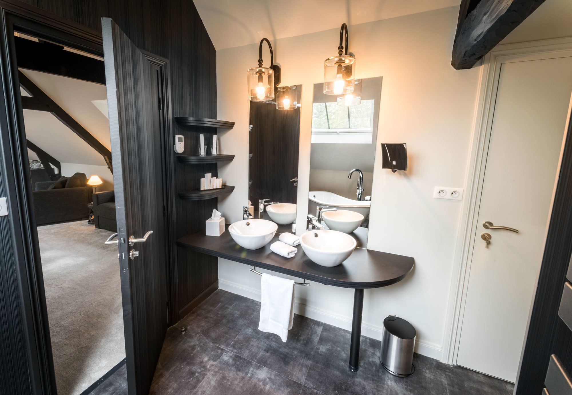 A modern bathroom with dark wood cabinetry, a black countertop, three white sinks, and pendant lighting.