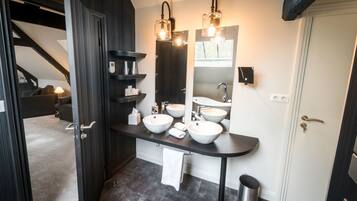 A modern bathroom with dark wood cabinetry, a black countertop, three white sinks, and pendant lighting.