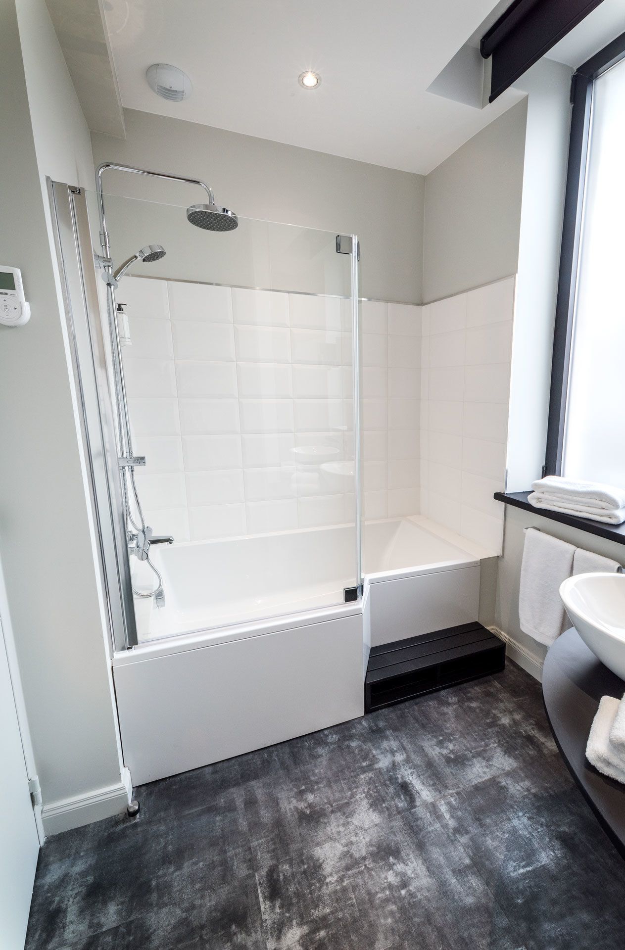 Un baño moderno con ducha envuelta en vidrio, una bañera blanca, encimera negra y lavamanos blanco.