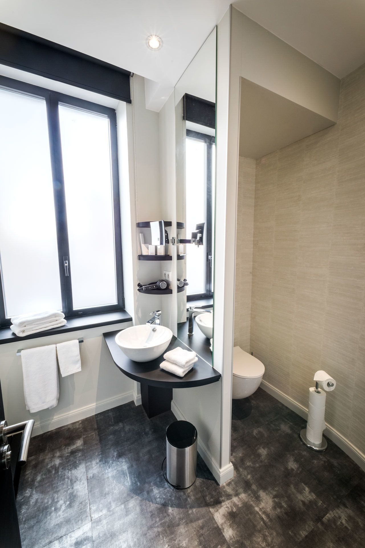 Ein modernes Badezimmer mit großem Fenster, einem runden Waschbecken, einer Toilette und einem Spiegel.