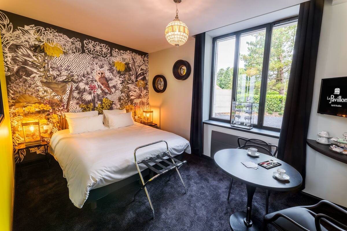A hotel room with a bed, bedside table, and a window with a view of trees.