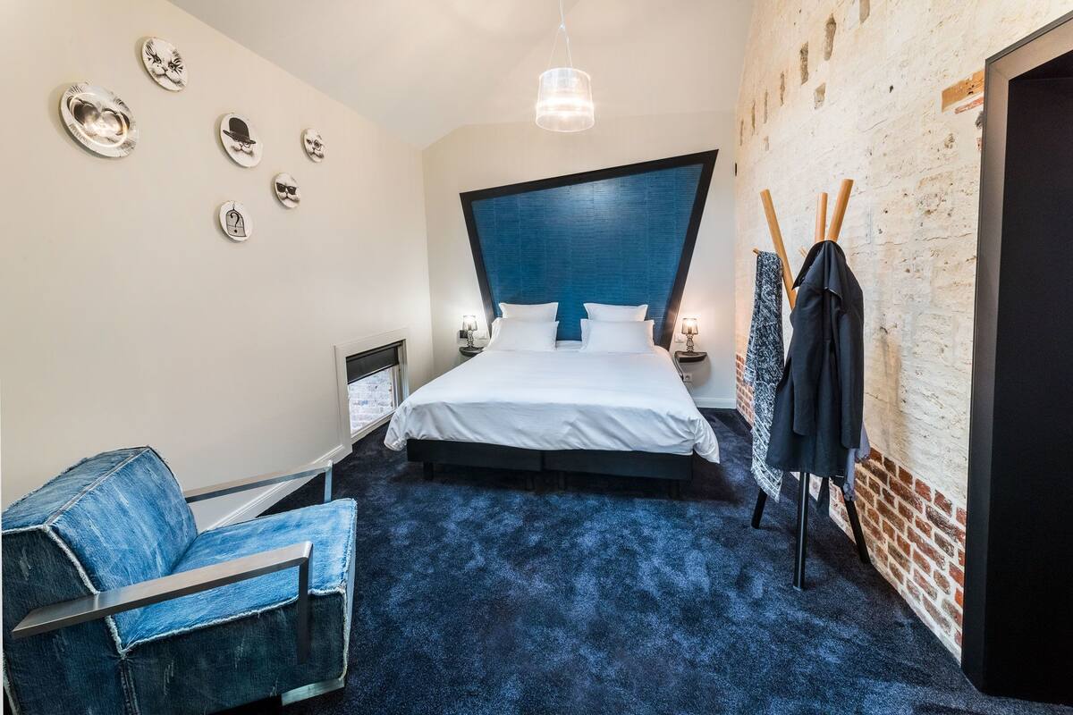 A modern bedroom with a large bed, a blue headboard, a blue carpet, and a denim chair.