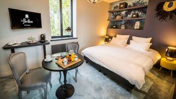 Ein Hotelzimmer mit Bett, Schreibtisch mit Frühstücksangeboten, Fernseher und Fenster mit Blick auf Bäume.