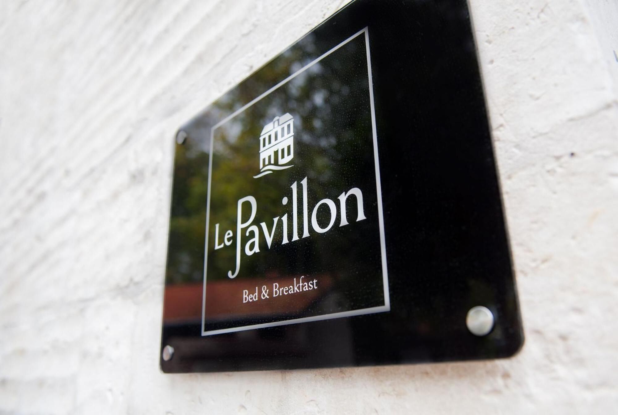 A black sign with white lettering that reads "Le Pavillon Bed & Breakfast" against a white wall.