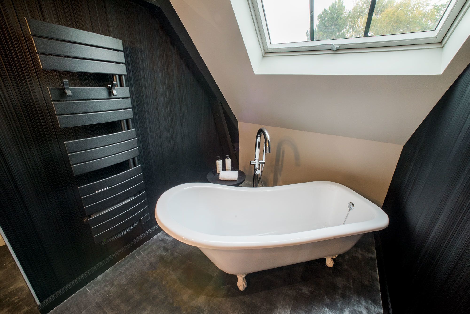 Un baño moderno con una bañera independiente, una ventana sobre el lavamanos y un panel de pared de madera oscura.