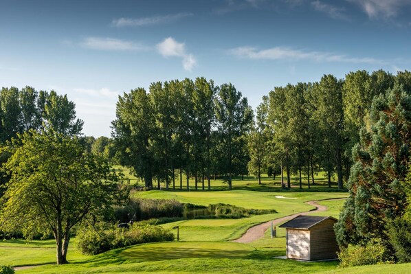 Un campo de golf con un cobertizo pequeño, rodeado de árboles frondosos y un cielo despejado.