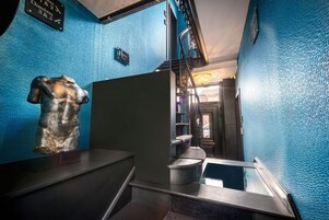 Una escalera con un muro azul con textura, una escultura de metal y un cartel con indicaciones de números de habitaciones.