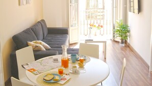 Un comedor con una mesa redonda, sillas y un sofá. Hay una planta en maceta y vistas al balcón exterior.