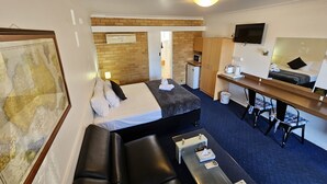 A compact hotel room with a bed, a desk, a small kitchenette, a TV, and a map on the wall. - Hunter Valley Motel (Cessnock)