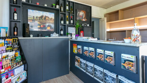 A bar area with shelves of wine bottles, a television, and magazines on the wall. - Hunter Valley Motel (Cessnock)
