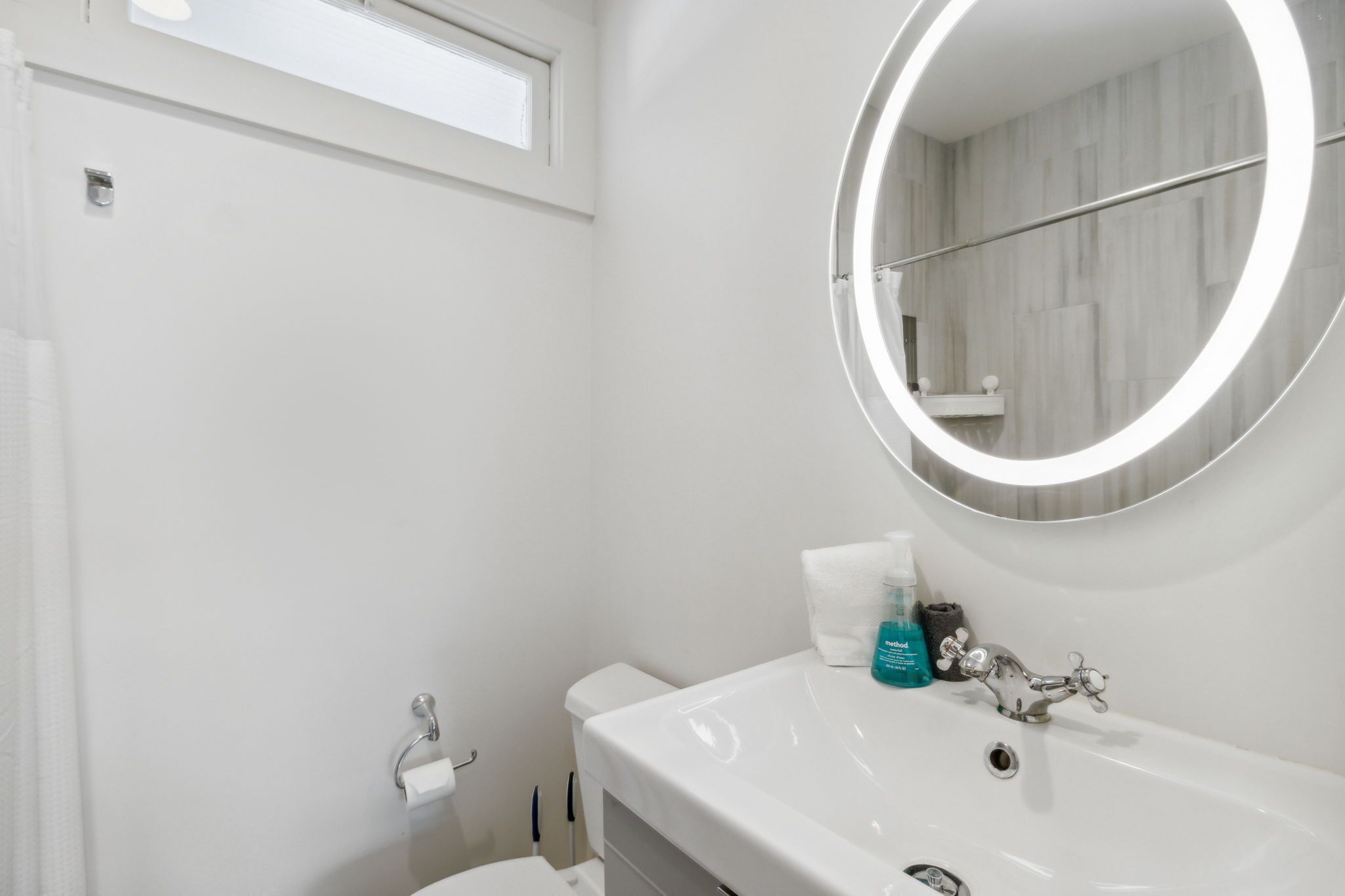 Een badkamer met een witte wasbak, een spiegel met verlichting en een toilet.