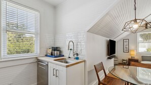 Une cuisine moderne avec des meubles blancs, un lave-vaisselle encastré et un coin repas comprenant une table en verre et des chaises en bois.