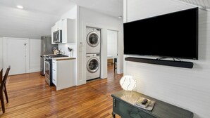 A compact living space with a kitchen, a washing machine, a microwave, and a flat-screen TV mounted on the wall. - Stanton Apartment C - Historic retreat 1 block to beach (Saint Simons Island)