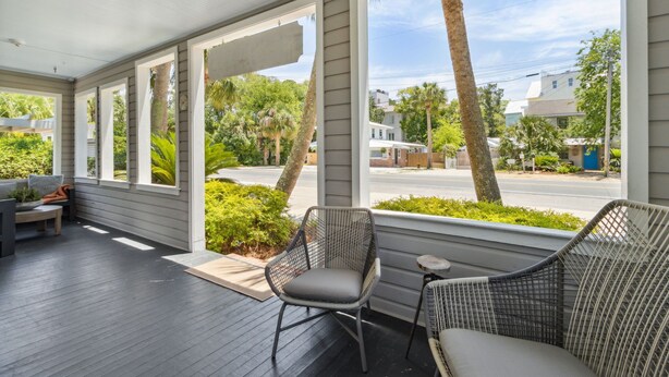 A covered porch with a view of the street, featuring wicker chairs and a bench. - Stanton Apartment C - Historic retreat 1 block to beach (Saint Simons Island)