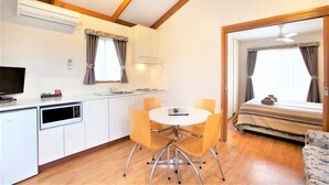 A compact hotel room with a kitchenette, a dining area with a round table and chairs, a bed with a view, and a small seating area.