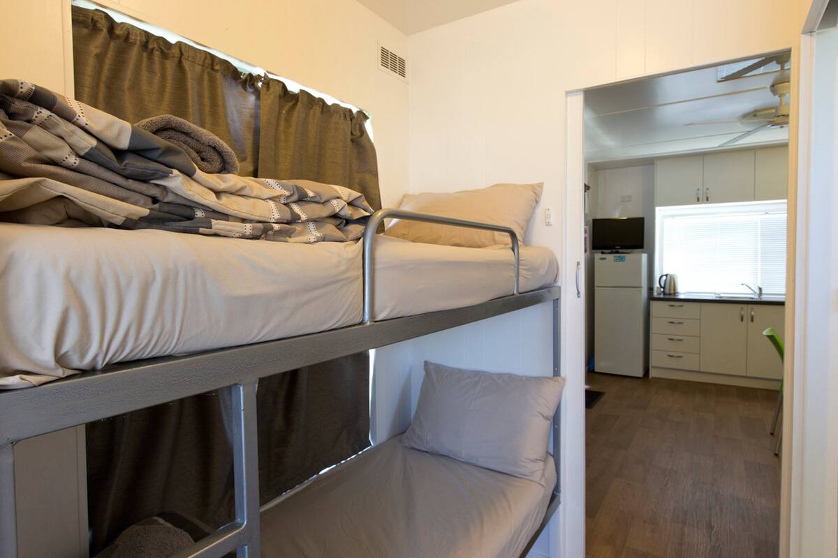 A bunk bed with a kitchen area visible through an open door.