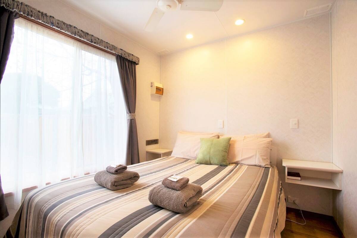 A hotel room with a bed, a nightstand, a wall-mounted shelf, and a window with curtains.