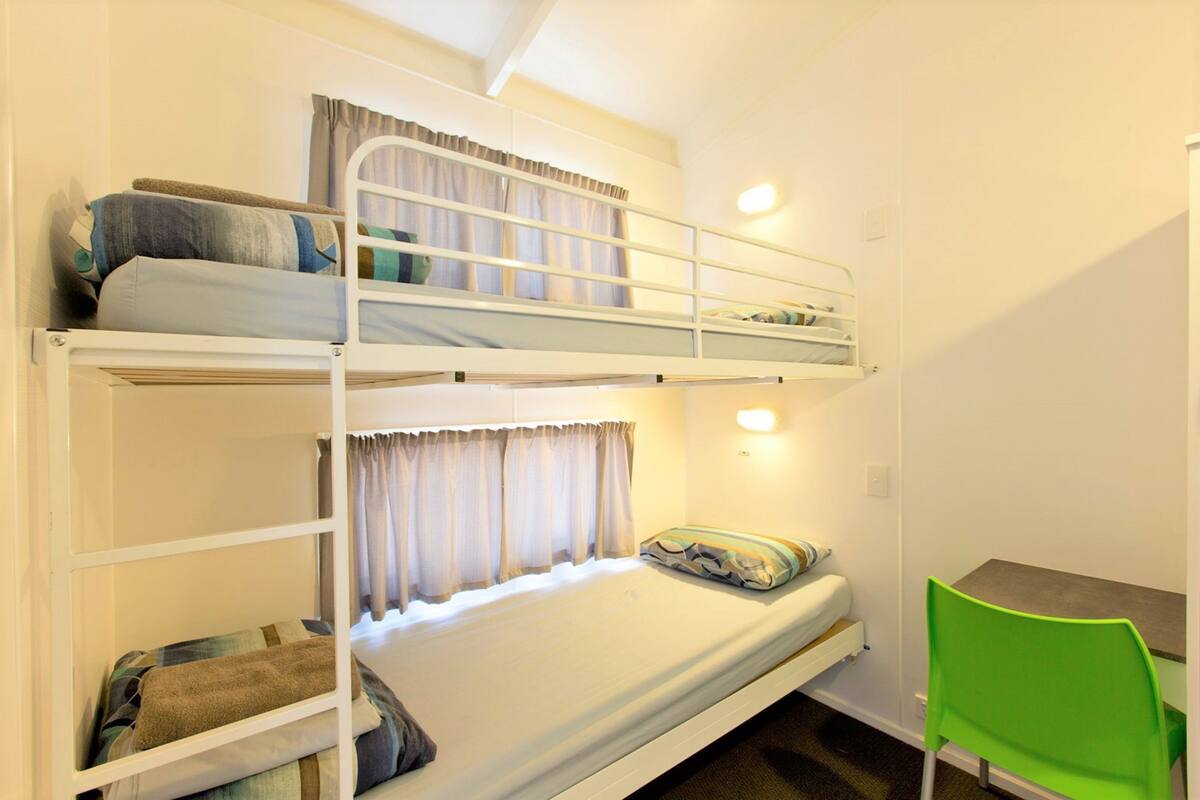 A bunk bed room with a desk and chair, curtains, and a light fixture.
