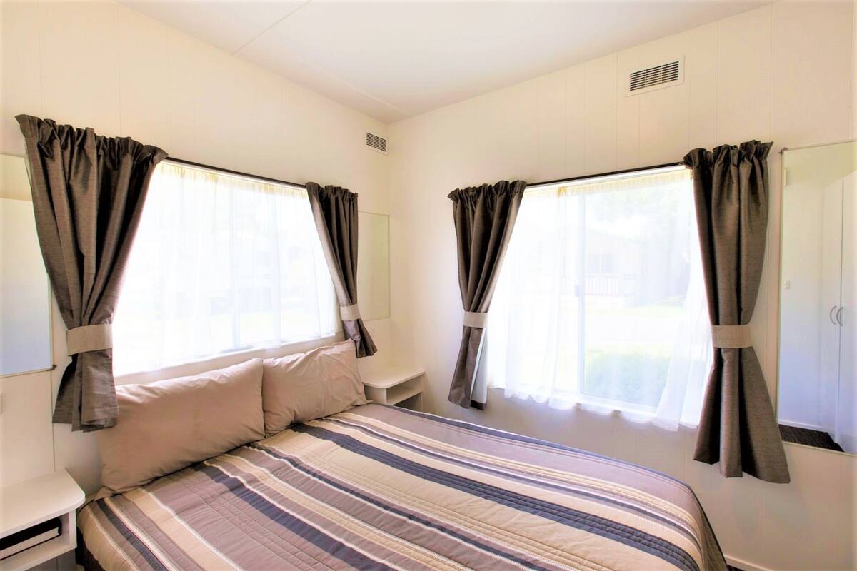 A bedroom with a bed, curtains, a bedside table, and a wardrobe.