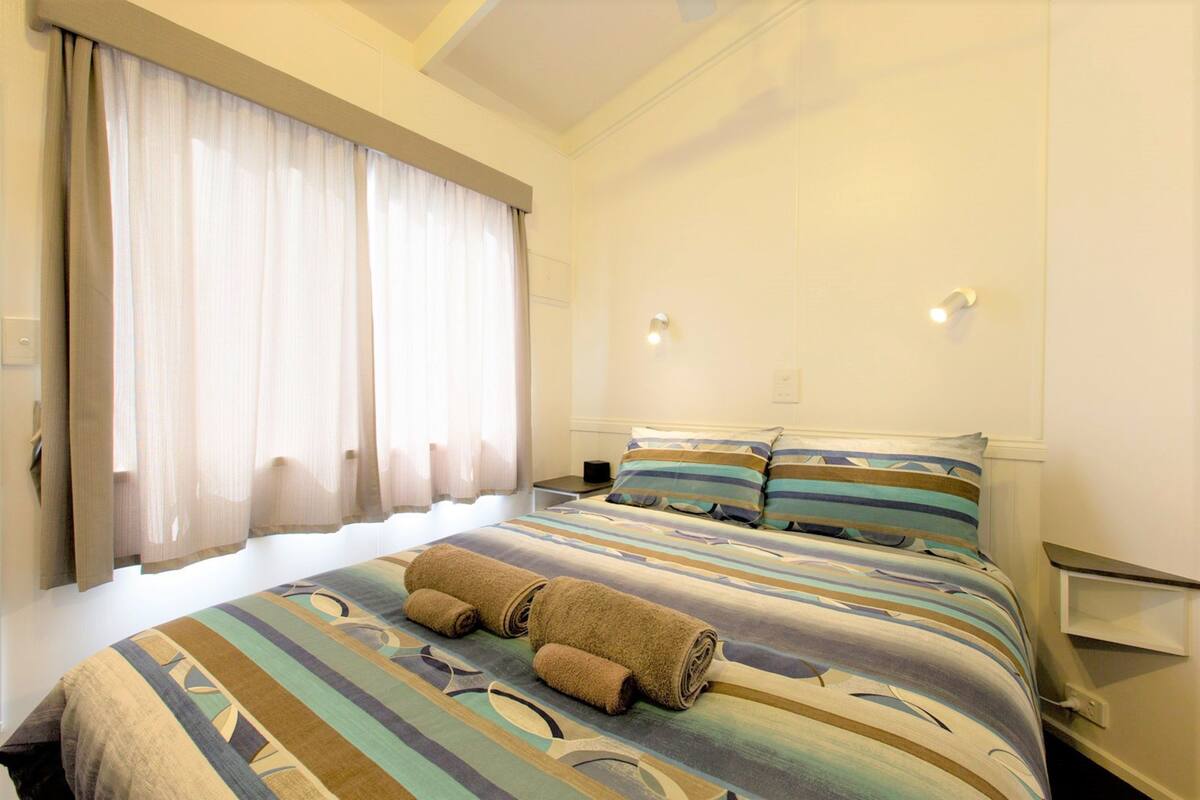 A hotel room with a large bed, a nightstand, a lamp, and a window with curtains.