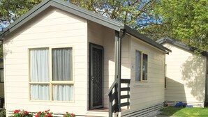 A single-story mobile home with a front porch, a small set of steps, and a window with curtains.