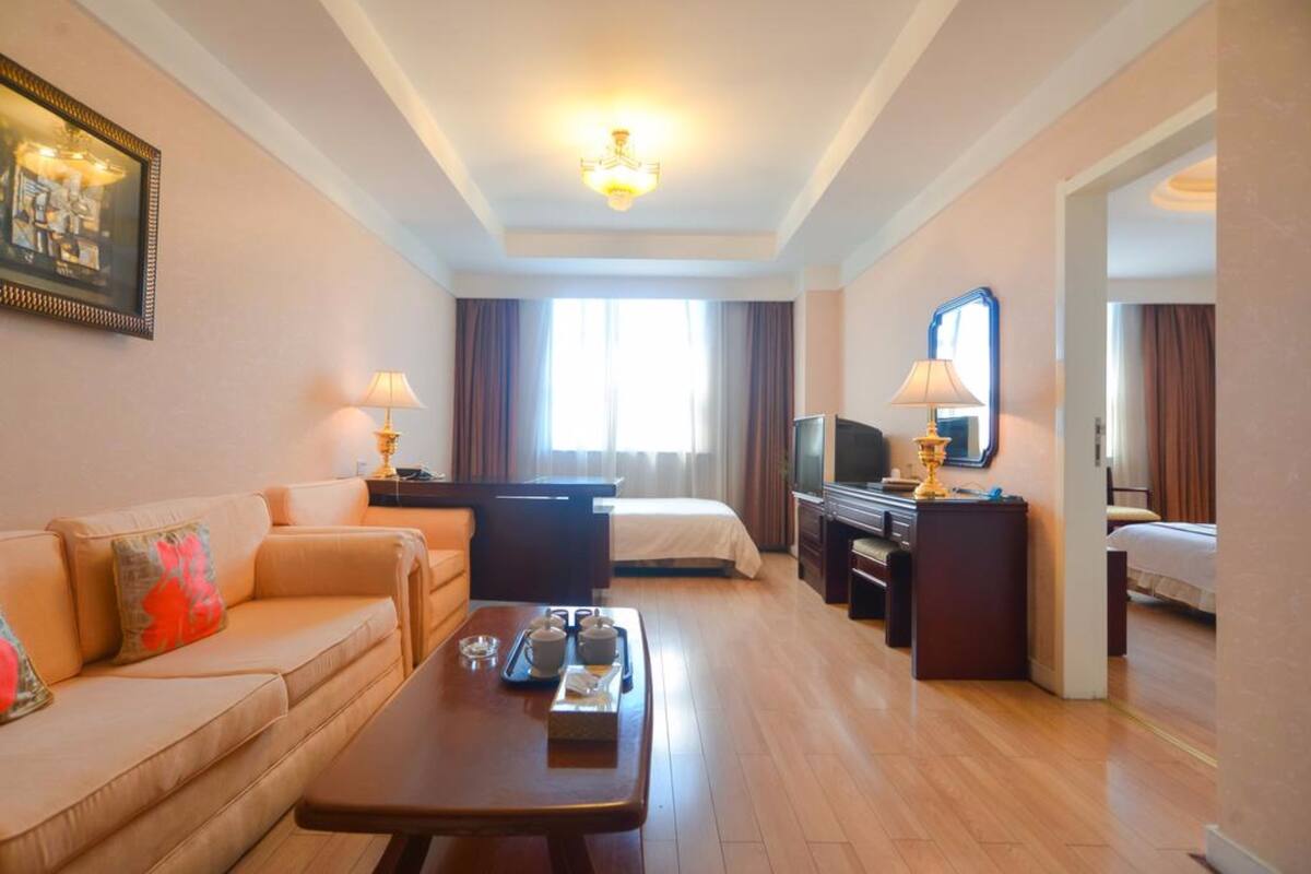 Ein Hotelzimmer mit Sofa, Bett, Schreibtisch mit Fernseher und Esstisch mit Tablett.