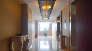 A hallway with a chandelier, a potted plant, and a trash bin. - Yangcheng Hotel (Qinhuangdao)