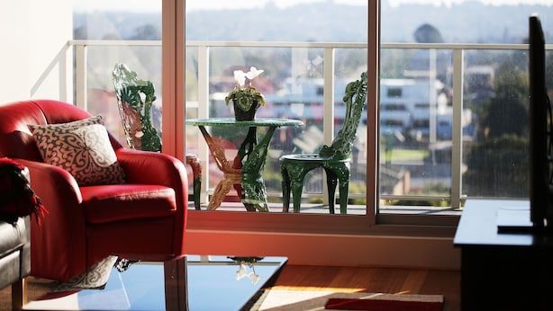 A modern living room with a red sofa, a glass coffee table, and a view of the city through large windows. - Bluebell Apartments (Box Hill)