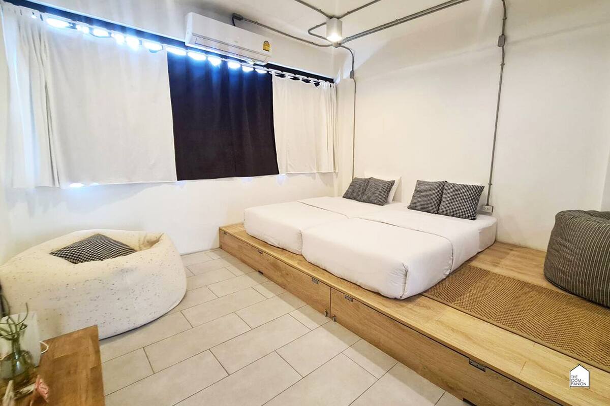 A modern bedroom with a bed, a small seating area, and a window with curtains.