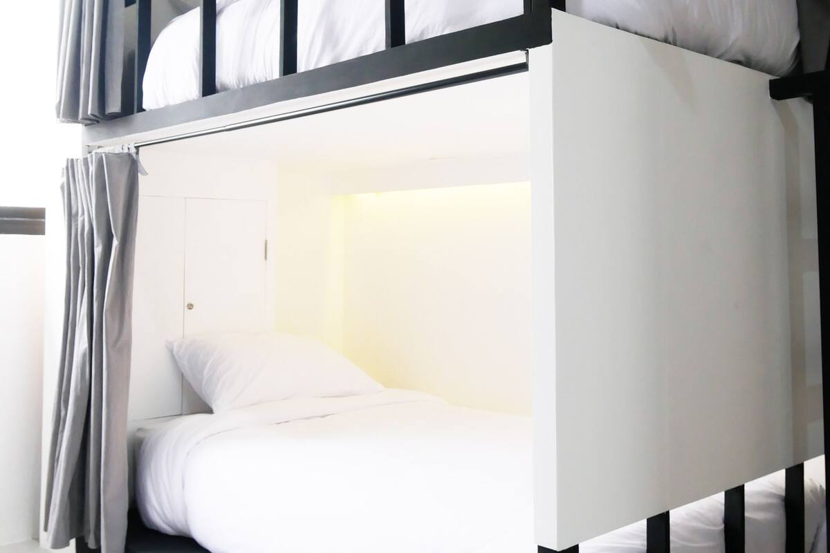 A bunk bed with white bedding and grey curtains.