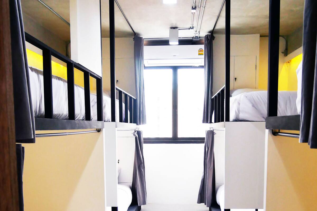 A narrow corridor with bunk beds on either side, a central walkway, and a window at the end.
