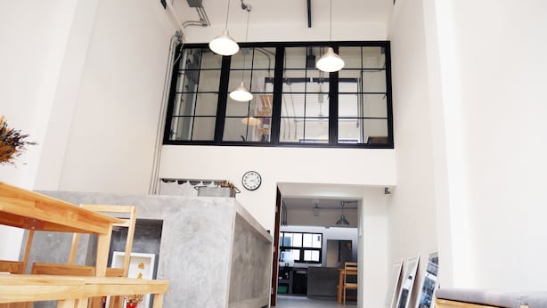 A spacious loft-style room with a high ceiling, exposed ductwork, and large windows. - The Companion - Hostel (Bangkok)
