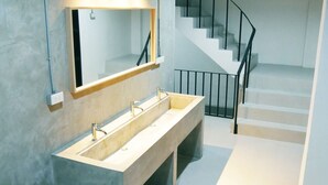 A modern bathroom with a large sink, a mirror, and a staircase leading to another floor. - The Companion - Hostel (Bangkok)
