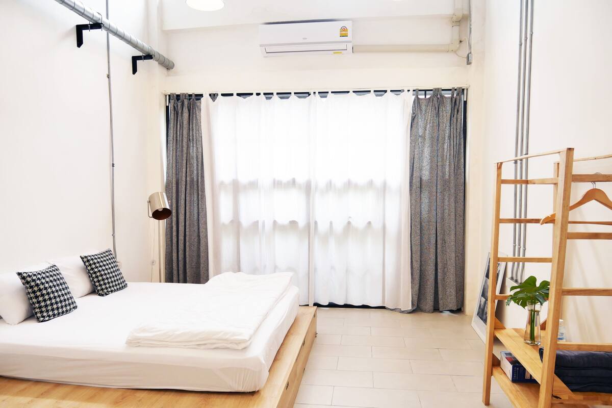 A bedroom with a bed, a wooden ladder, a potted plant, and a window with curtains.