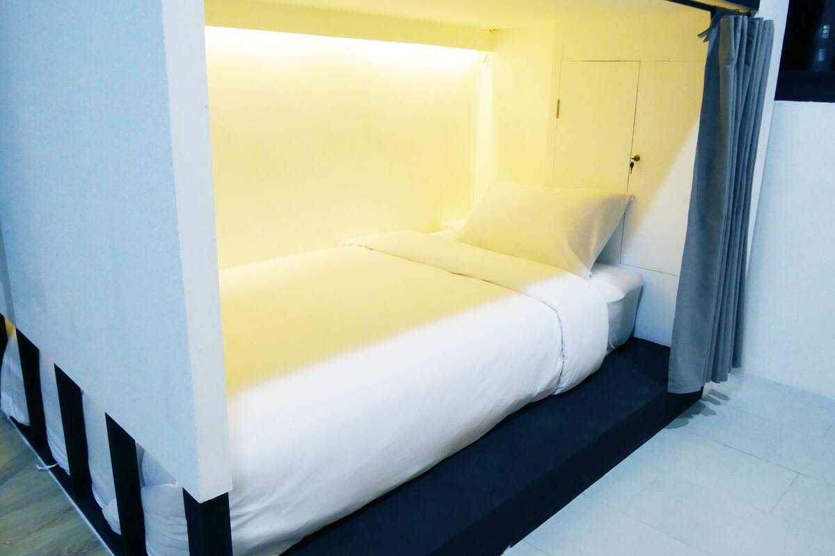A single bed with a white mattress and pillows, a black headboard, and a grey curtain.