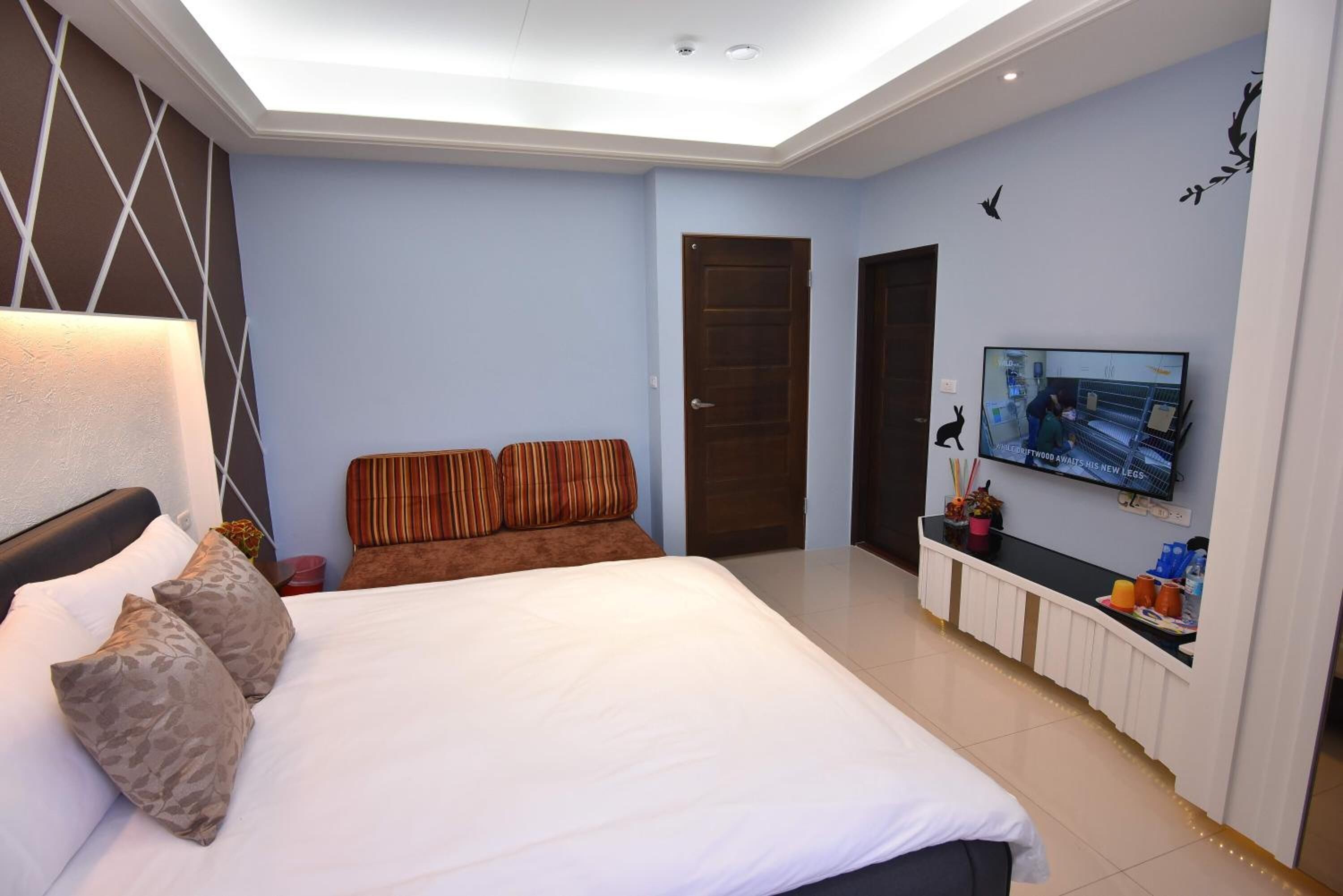 A bedroom with a large bed, a TV mounted on the wall, and a bedside table with a lamp.