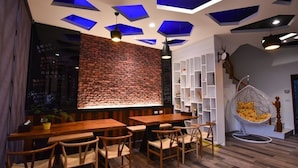 L’intérieur d’un restaurant avec des tables et des chaises en bois, un mur en briques, des luminaires bleus au plafond et un fauteuil suspendu agrémenté de coussins.