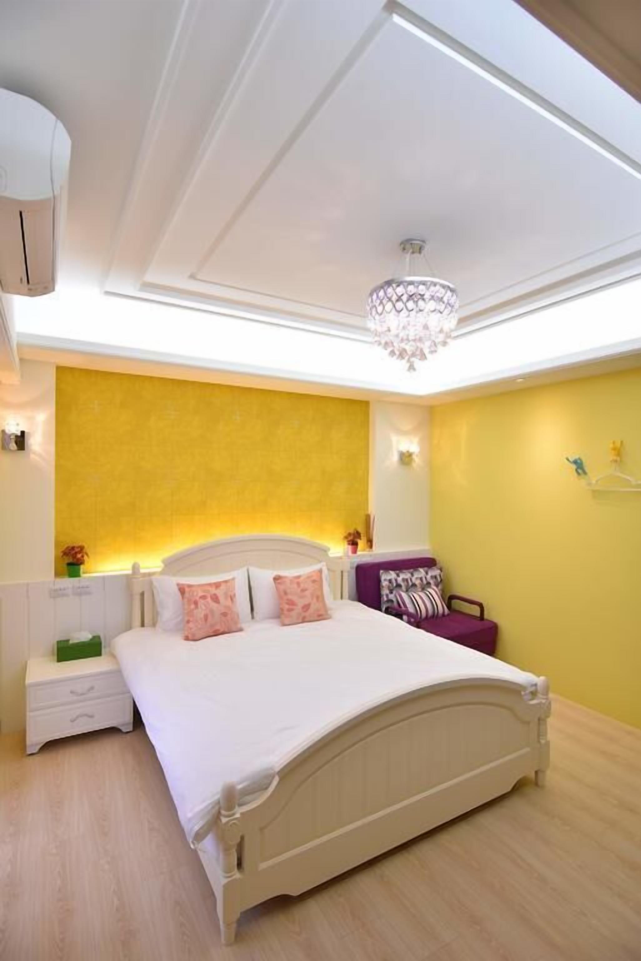 A bedroom with a bed, bedside tables, a nightstand, a chandelier, and a wall-mounted shelf.