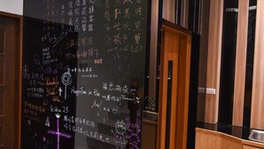 Un intérieur moderne avec un tableau noir couvert de notes et de dessins écrits à la main, un plancher en bois et un comptoir d’accueil.