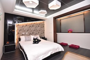 Una camera da letto moderna con una testiera a motivi geometrici, una decorazione con un gatto nero e una finestra vista città.