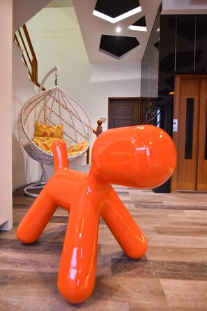 Un interno moderno con pavimento in legno, una poltrona amaca con cuscino e una scultura arancione brillante.