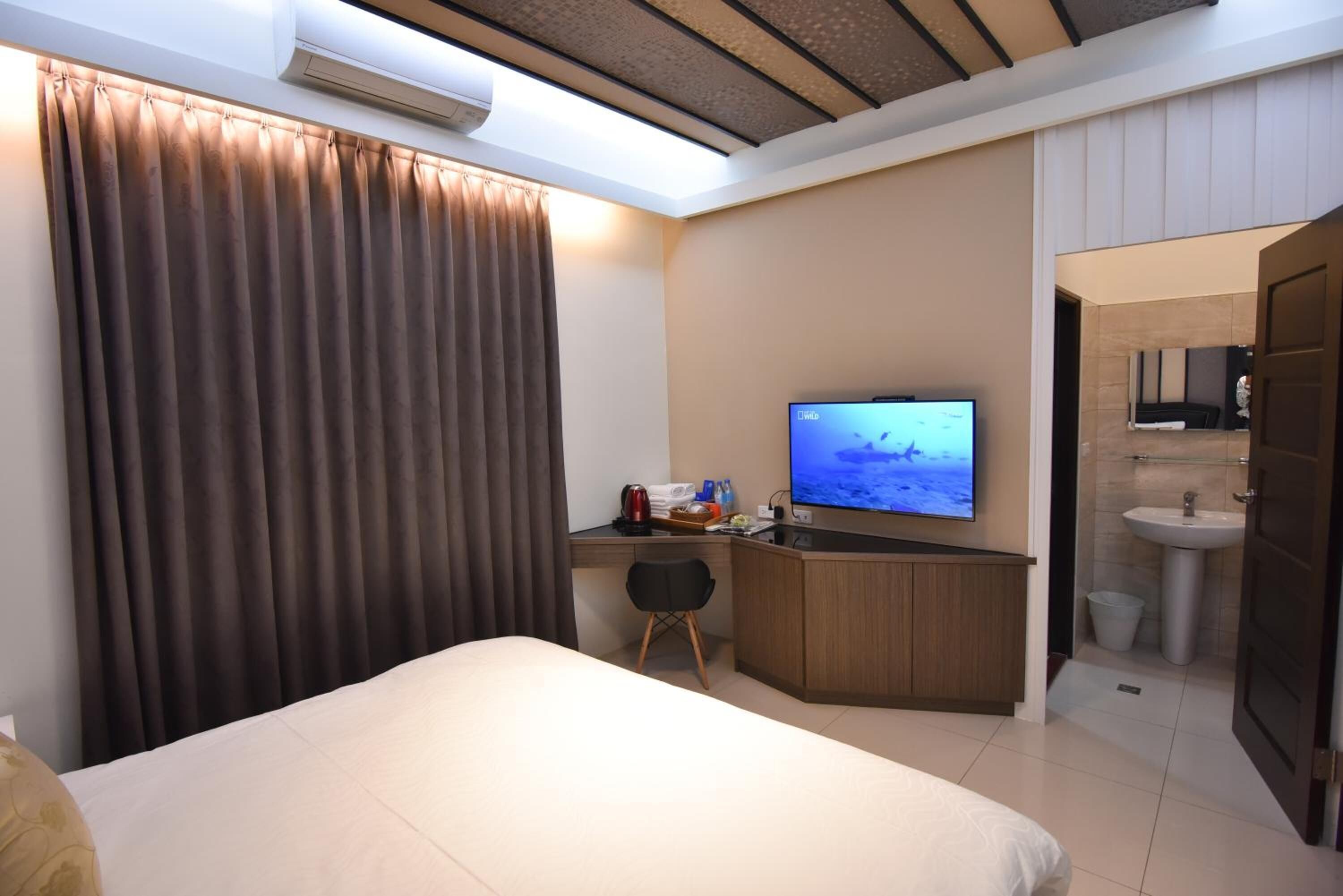 A hotel room with a bed, a desk with a television, a small chair, and a bathroom visible through an open door.